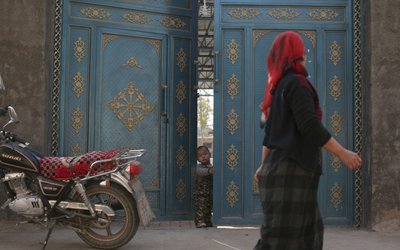 A child looks out from a door as a Uighur woman walks by in a residential area in Turpan, Xinjiang Uighur Autonomous Region