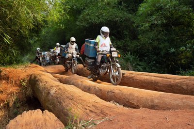 A motorcycle convoy carrying vials of measles vaccine and other supplies for medial NGO Doctors Without Borders crosses a log bridge on a road between Lisala and Boso-Manzi in Mongala province
