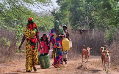 Women and a girl carry containers to fetch water from an abandoned stone quarry on a hot day in Badama village