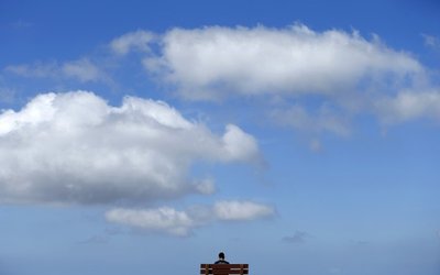 A young man sits high atop a hill reading a book on a park beach as the clouds pass overhead in San Marco, California