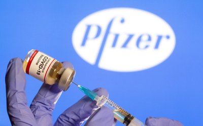 FILE PHOTO: A woman holds a small bottle labeled with a 'Coronavirus COVID-19 Vaccine' sticker and a medical syringe in front of displayed Pfizer logo in this illustration