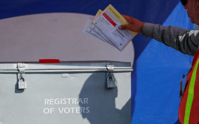 An election worker places mail-in ballots into an election box at a drive-through drop off location at the Registrar of Voters in San Diego, California