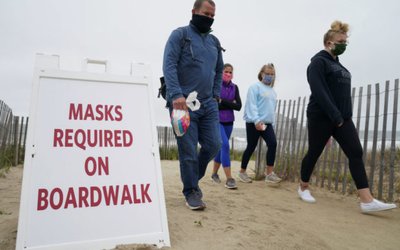 Vistors pass a face mask sign near the boardwalk at Bethany Beach in Delaware
