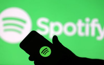 A smartphone is seen in front of a screen projection of Spotify logo, in this picture illustration