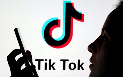 A person holds a smartphone as Tik Tok logo is displayed behind in this picture illustration