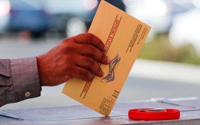 An election worker places a mail-in ballot into an election box at a drive-through drop off location at the Registrar of Voters in San Diego, California