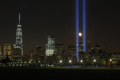 The moon rises between the "Tribute in Light" illuminated next to One World Trade Center during 911 anniversary, as seen from Jersey City, New Jersey