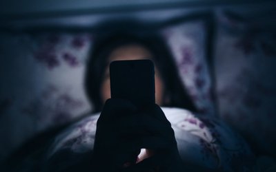 Woman reading and texting on smartphone in bed