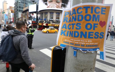 People walk past a "Practice Random Acts of Kindness" sign in Times Square Manhattan, New York