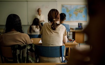 Rear view of teenage girls and boys learning in classroom