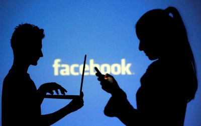FILE PHOTO: FILE PHOTO: People pose with laptops in front of projection of Facebook logo in this picture illustration taken in Zenica