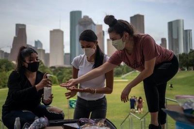 Mask wearing residents share hand sanitizer in front of skyline amid global outbreak of coronavirus disease in Houston, Texas